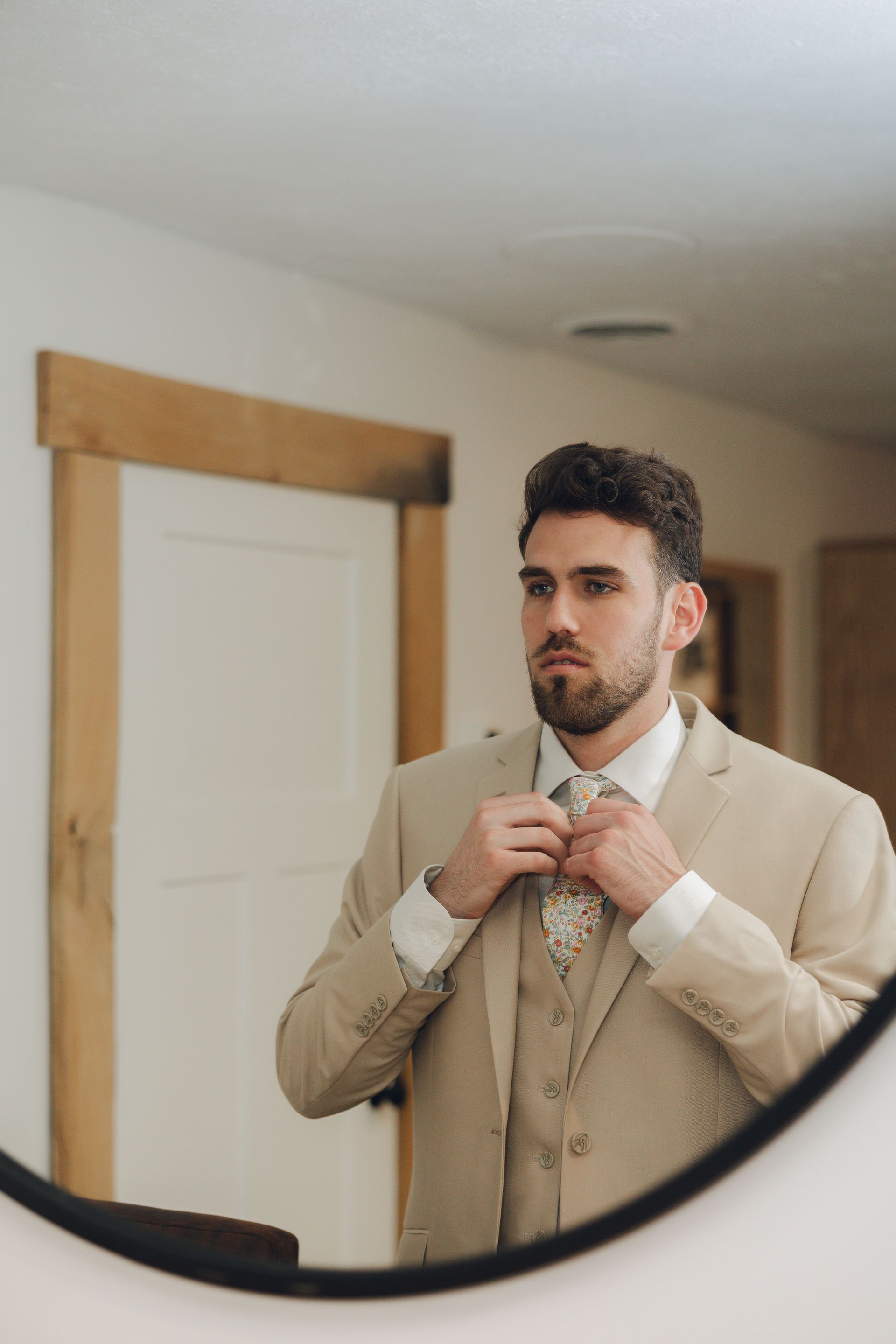 A man in a suit is adjusting his tie in front of a mirror.
