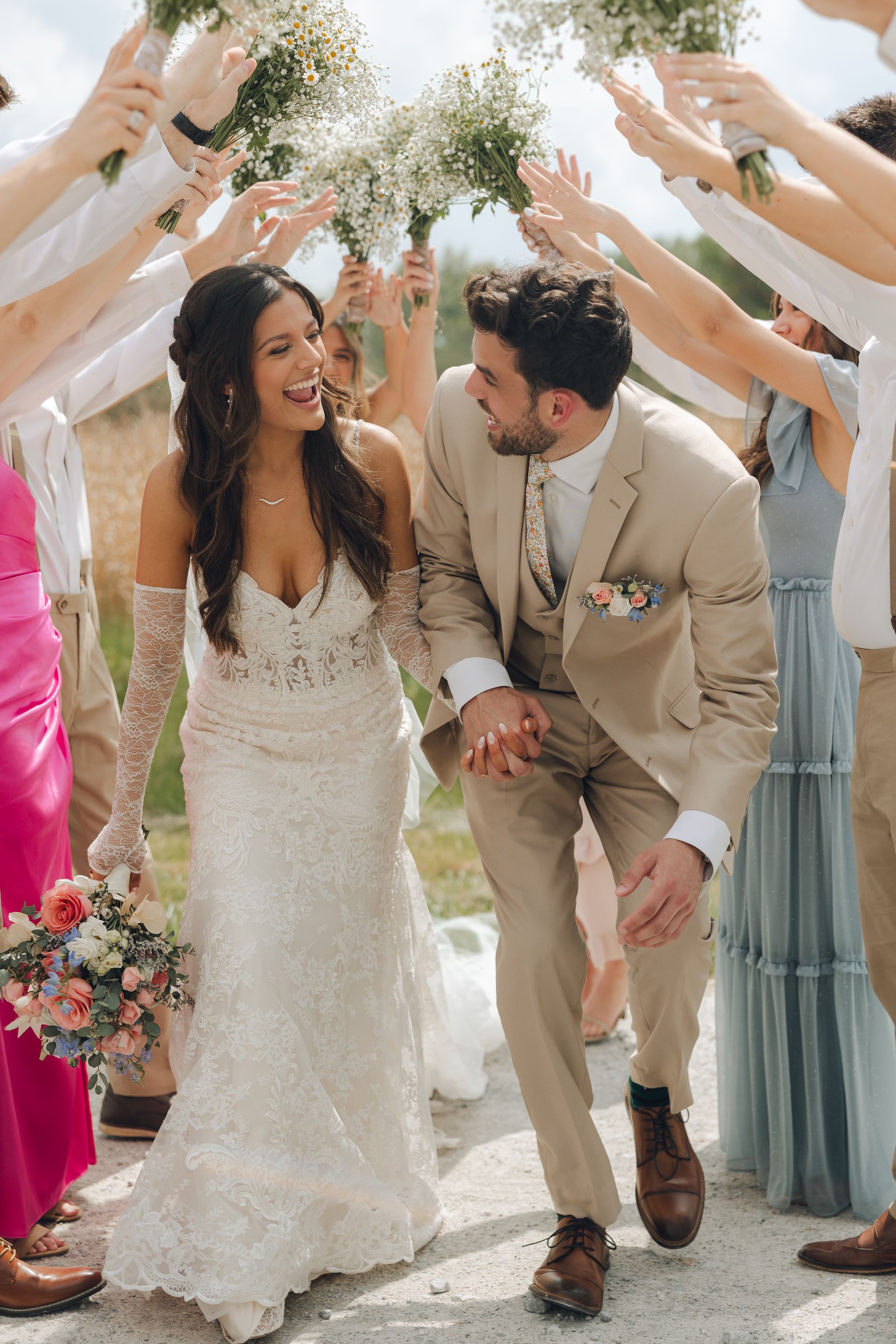 A bride and groom are walking through a crowd of people holding flowers.