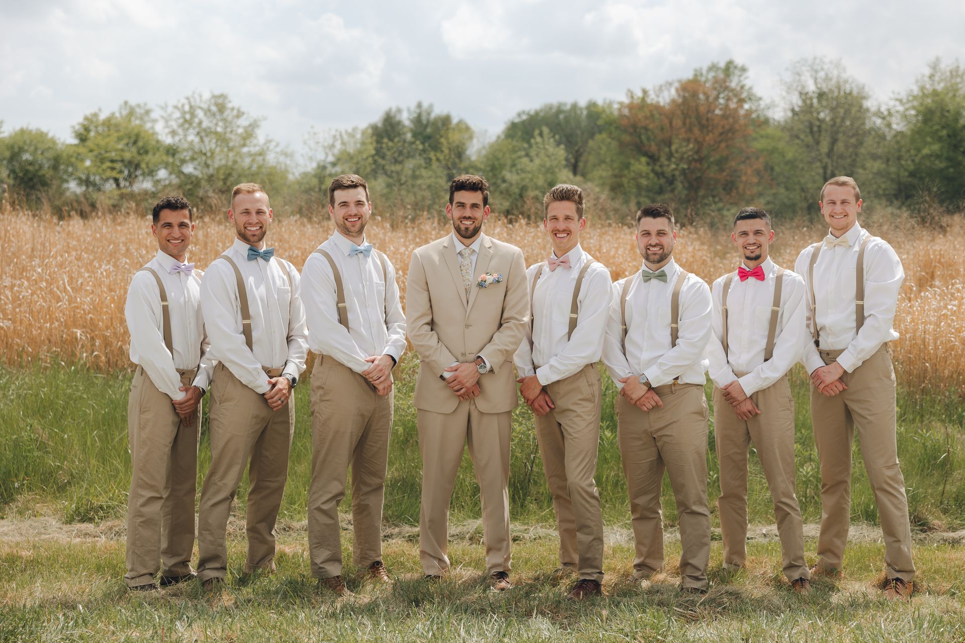 The groom and his groomsmen are posing for a picture in a field.