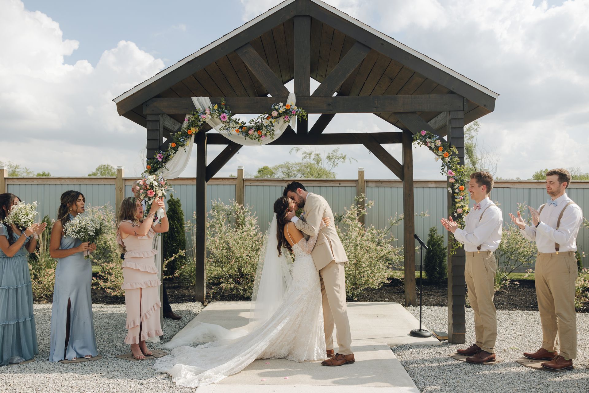A bride and groom are kissing under a gazebo at their wedding ceremony.