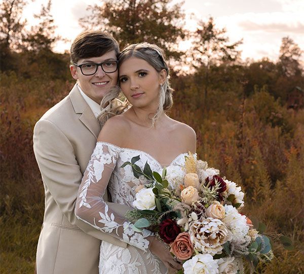 A bride and groom are posing for a picture while the bride is holding a bouquet of flowers.