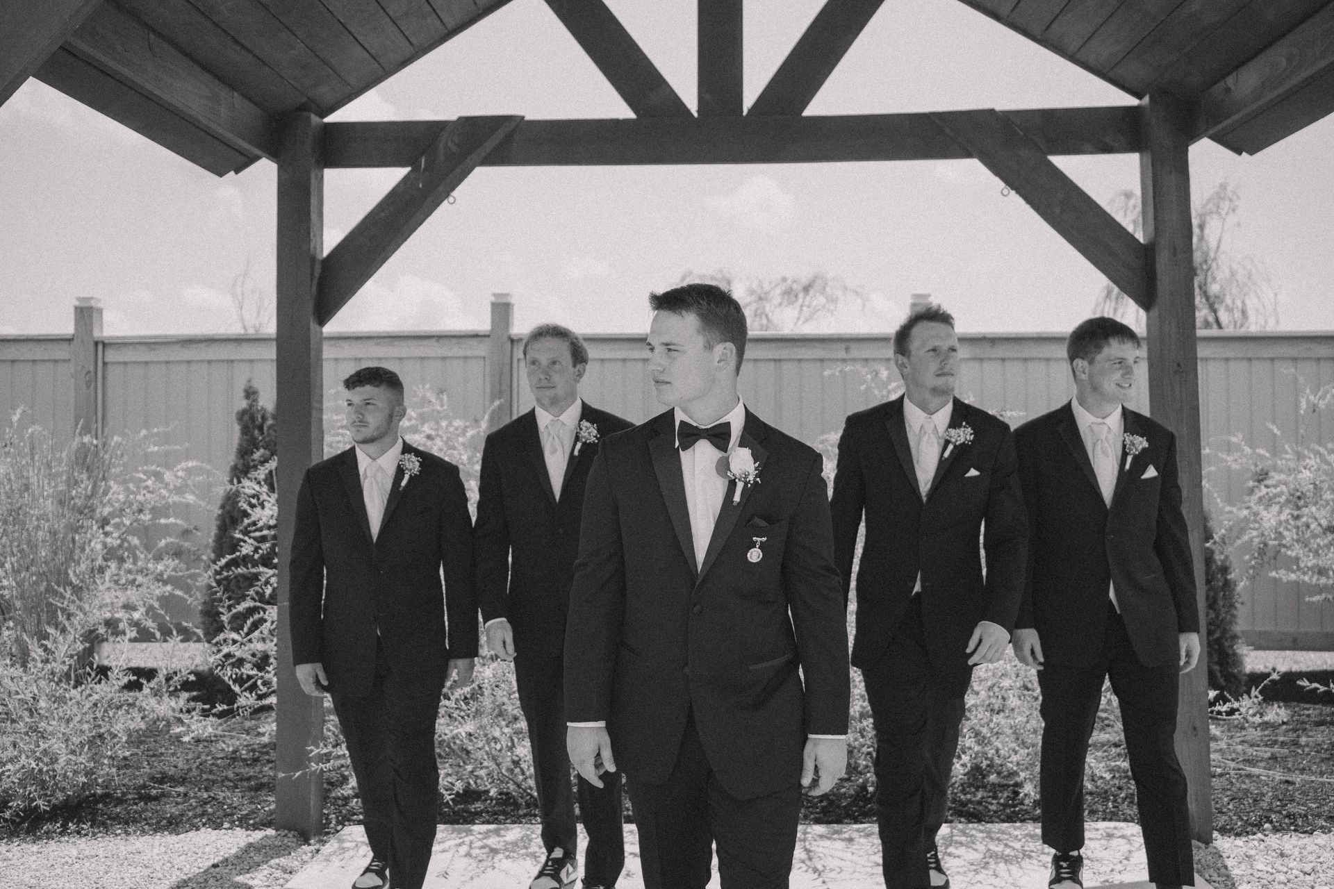 A black and white photo of a groom and his groomsmen walking under a canopy.