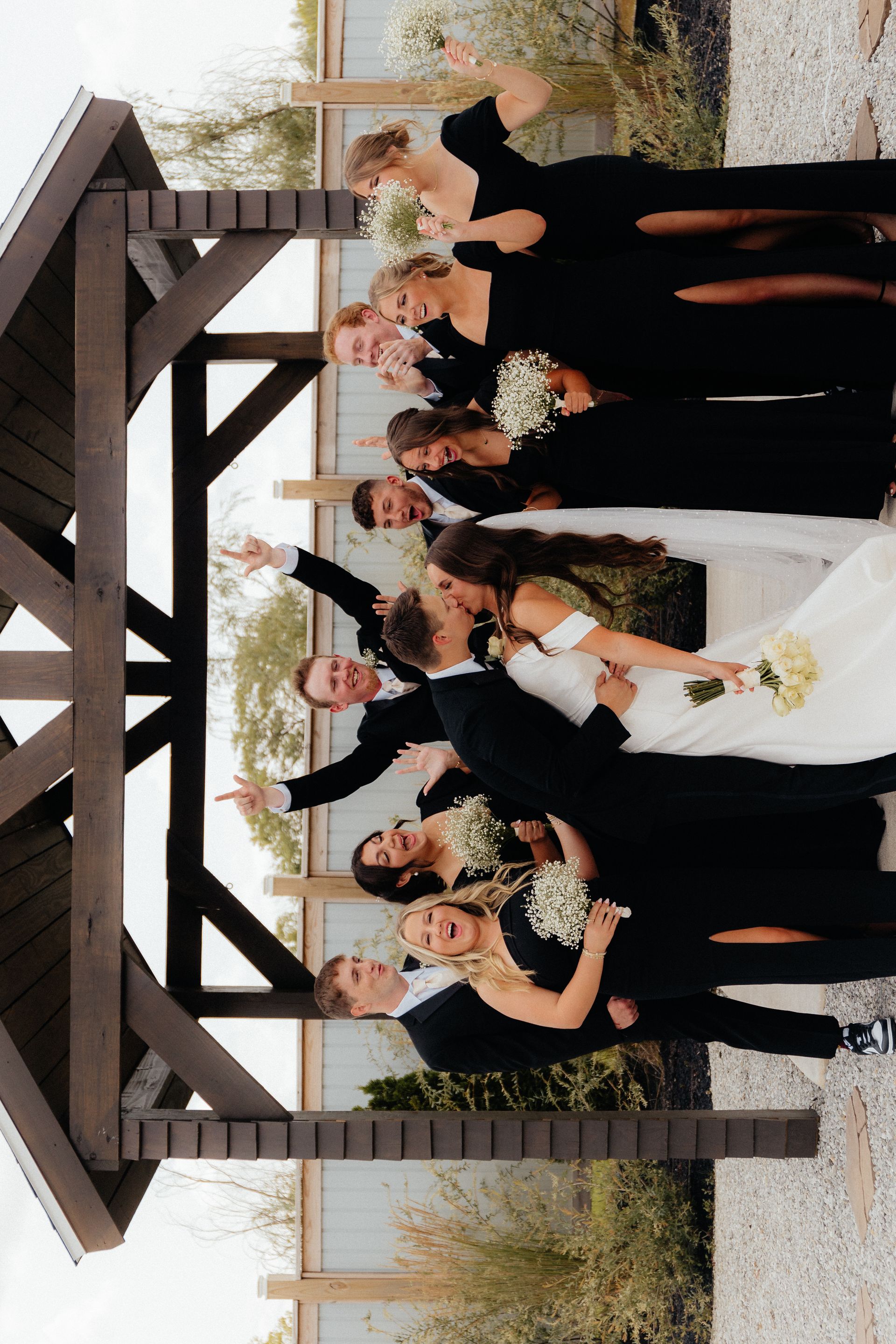 A bride and groom are posing for a picture with their wedding party under a gazebo.