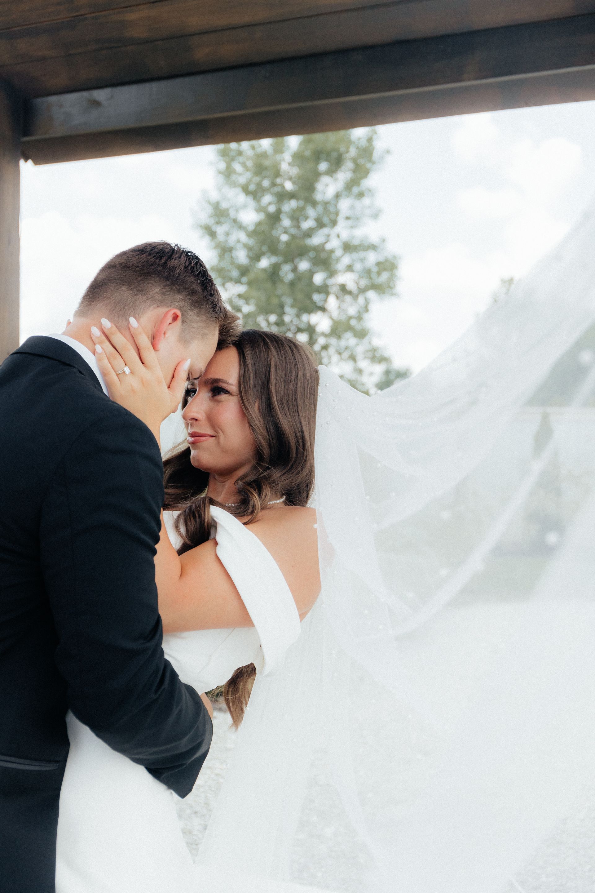 A bride and groom are kissing under a canopy with their veil blowing in the wind.