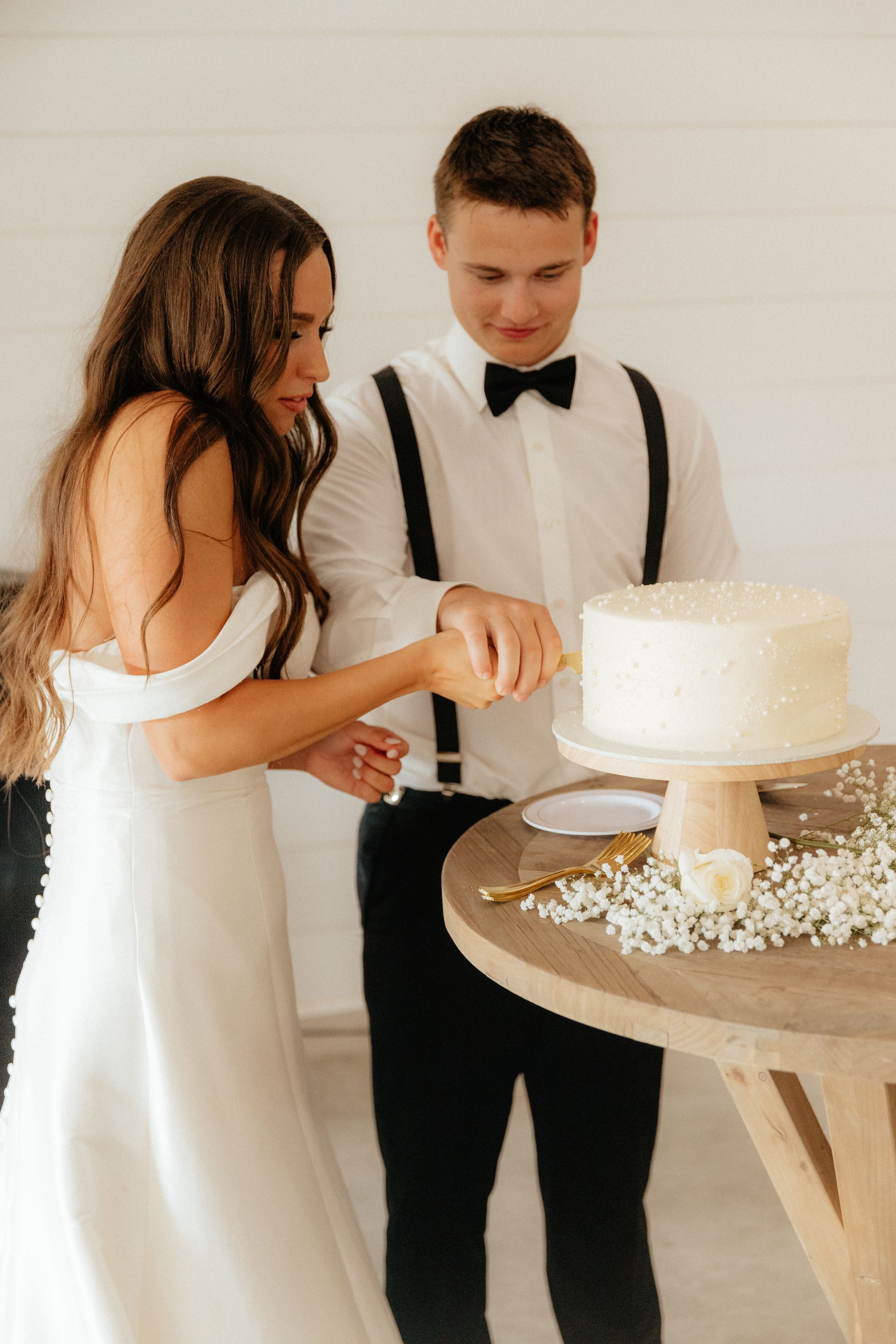 A bride and groom are cutting their wedding cake together.