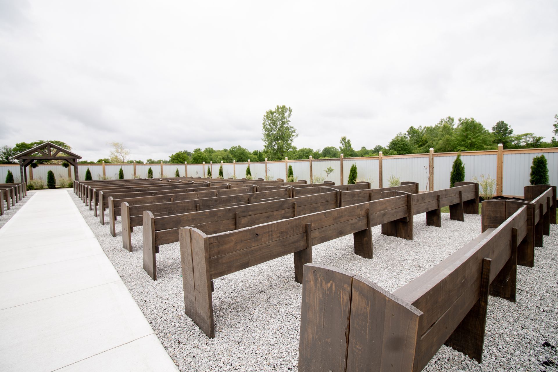A row of wooden benches are lined up in a gravel area.