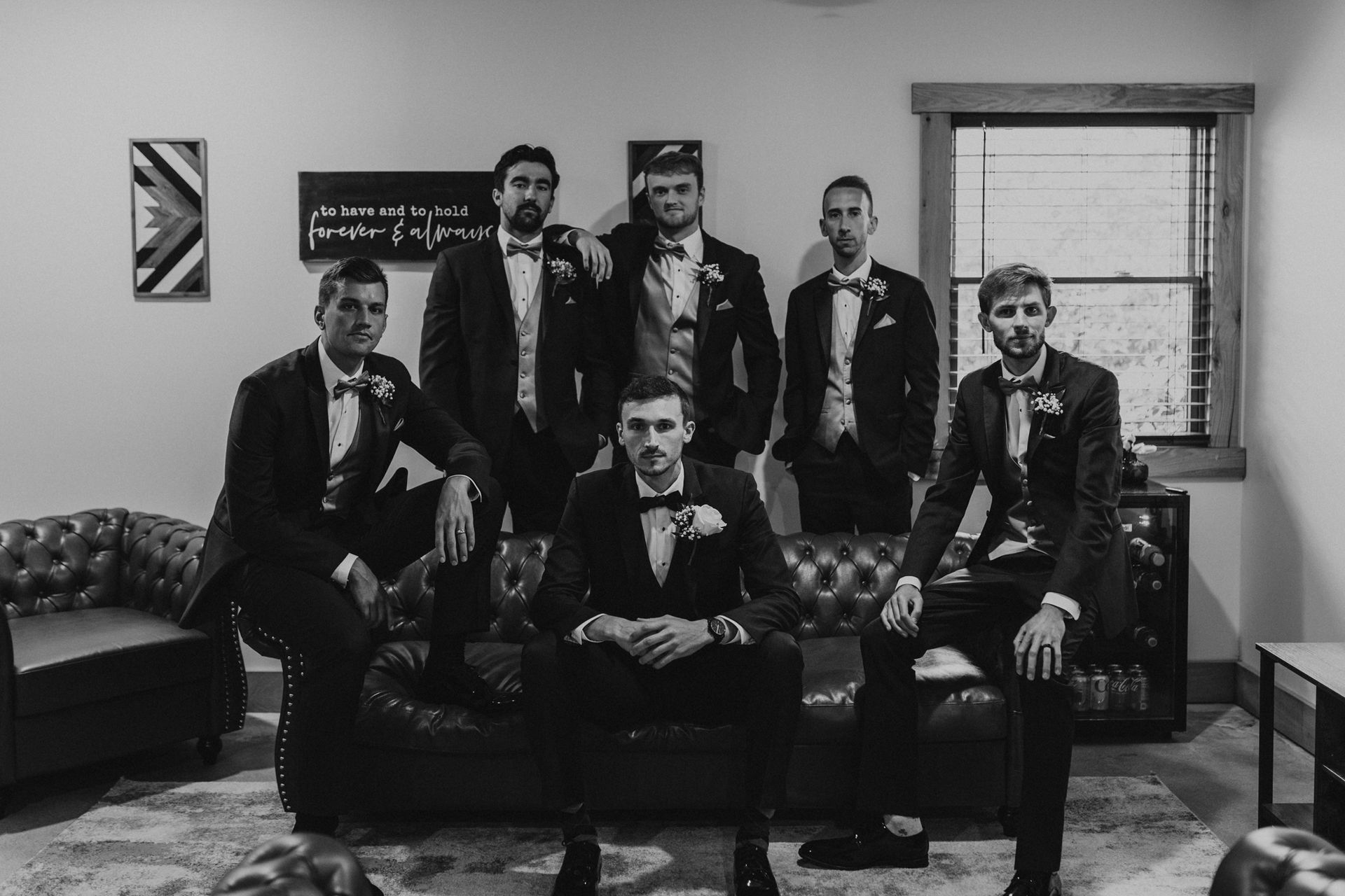 A group of men in tuxedos are posing for a picture while sitting on a couch.