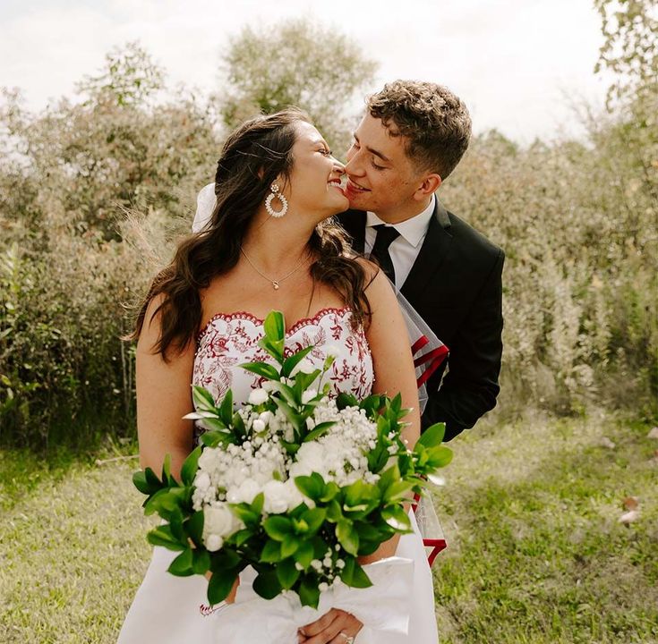 A bride and groom are kissing in a field while the bride is holding a bouquet of flowers.