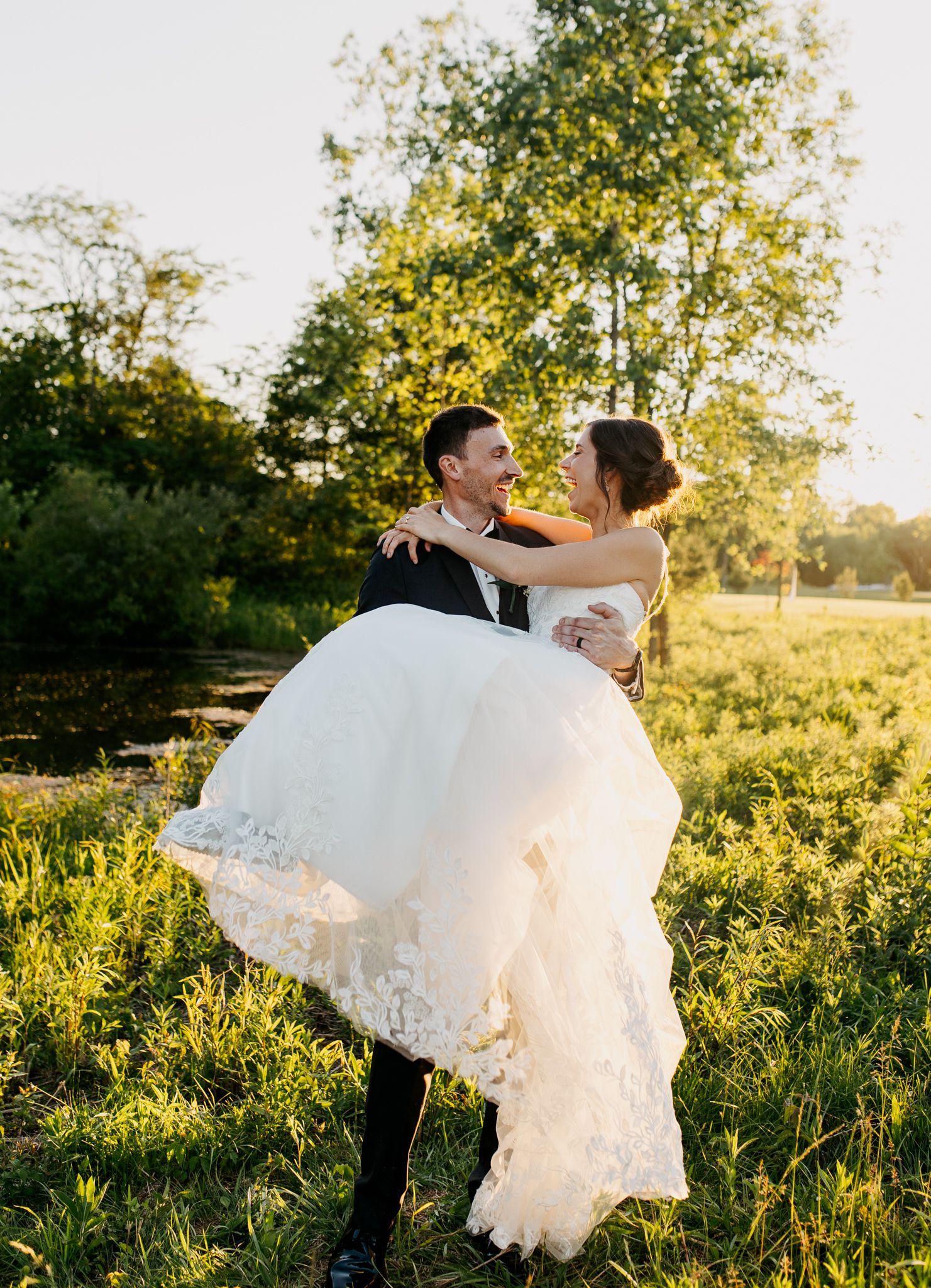 A man is holding a bride in his arms in a field.