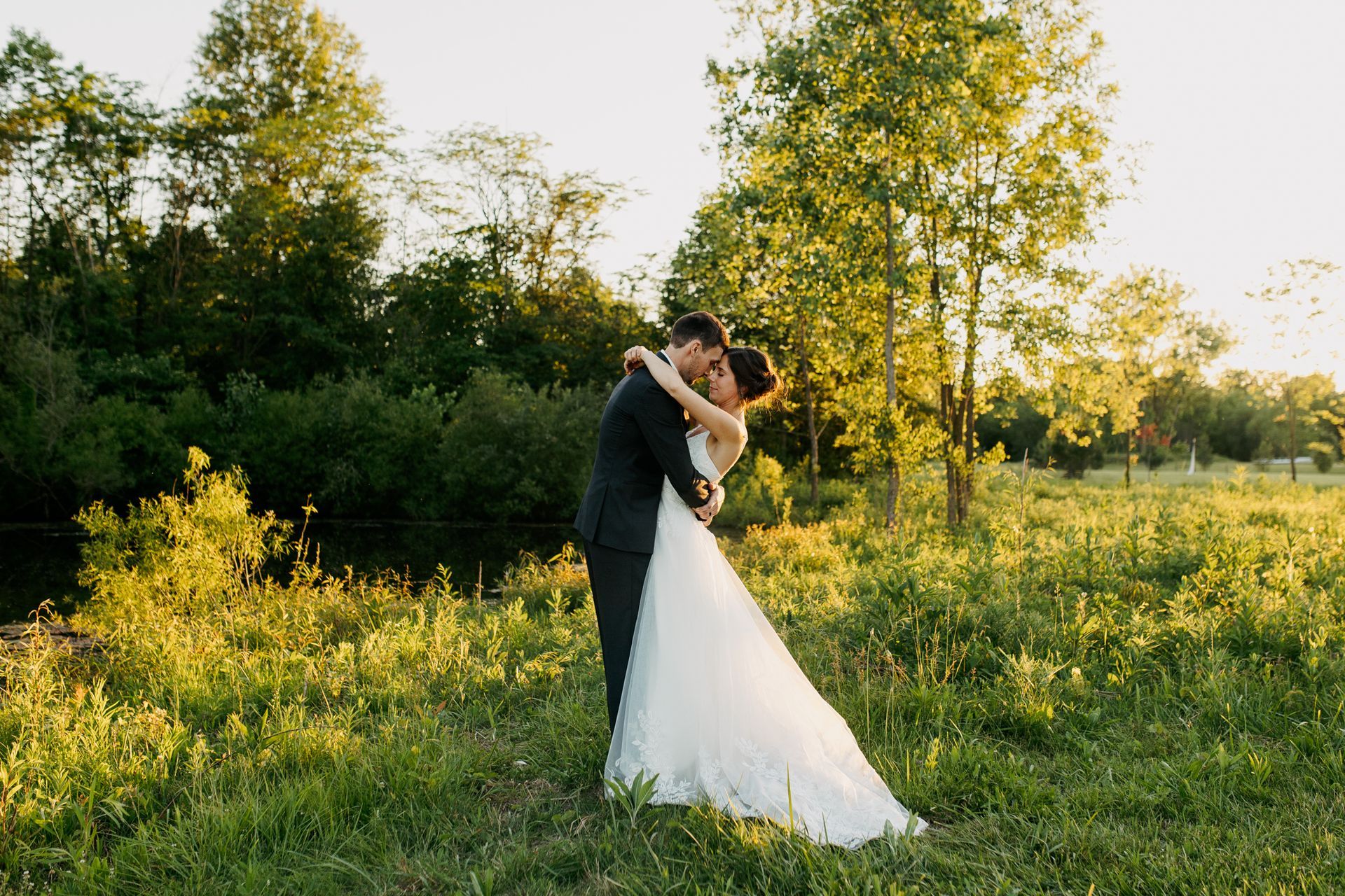 A bride and groom are kissing in a grassy field.