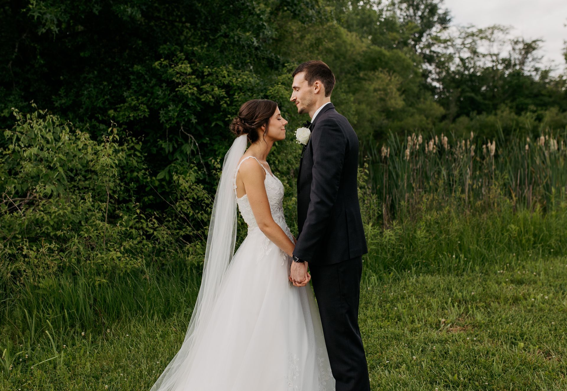 A bride and groom are standing in a field holding hands and looking at each other.