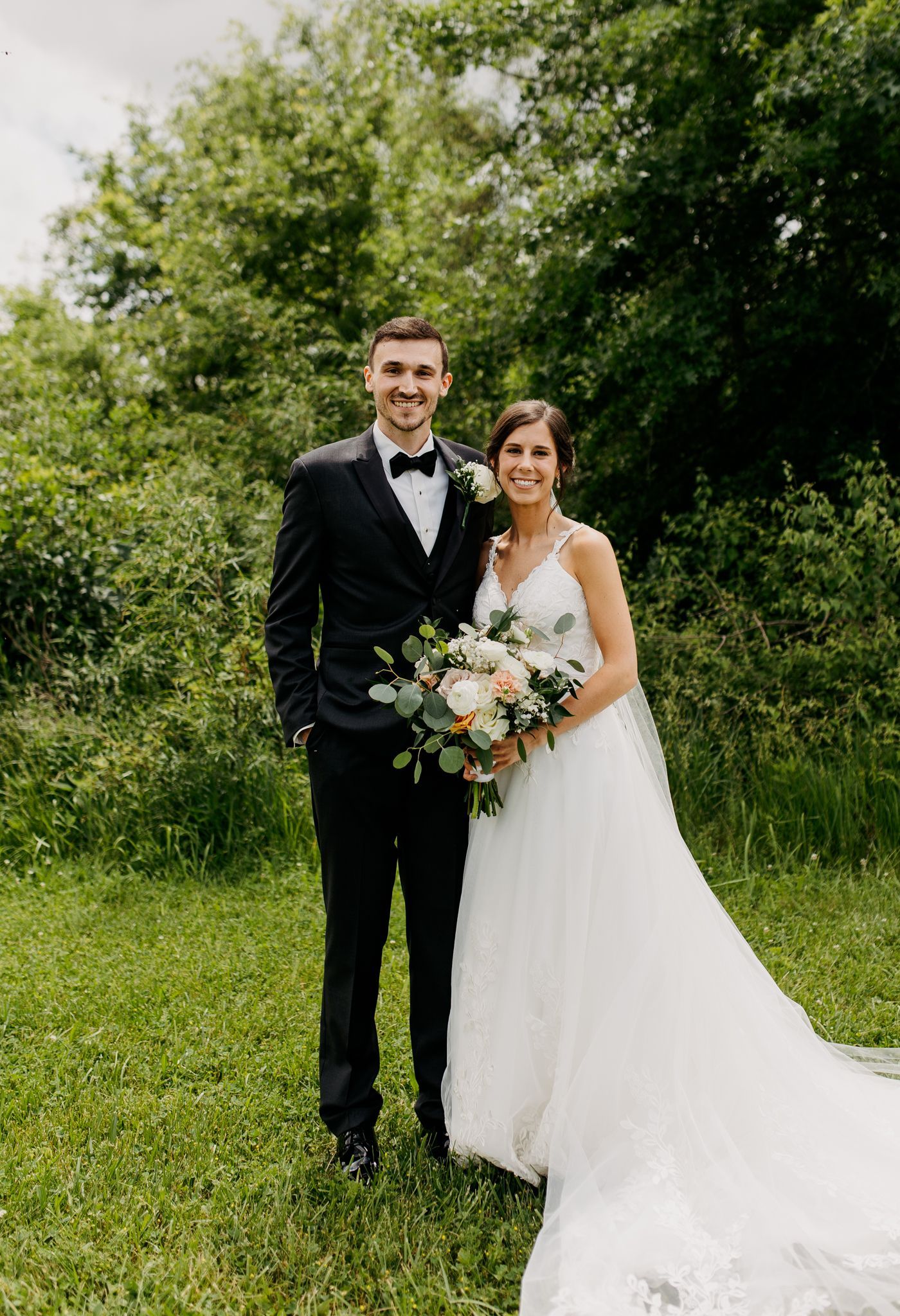 A bride and groom are posing for a picture in the grass.