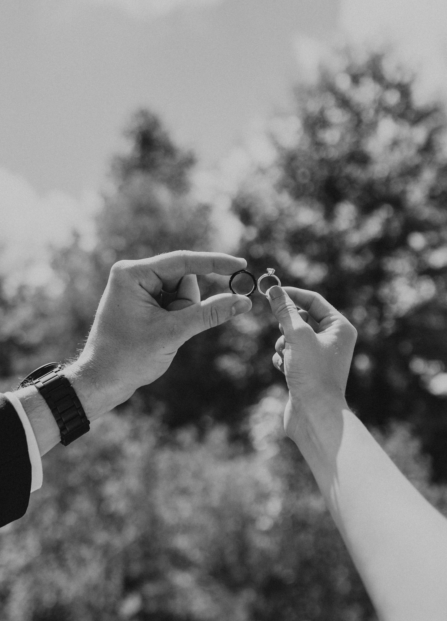 A black and white photo of a bride and groom holding their wedding rings.