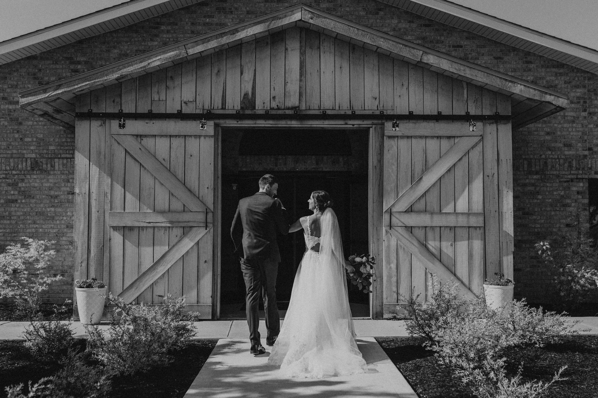 A black and white photo of a bride and groom walking into a barn.