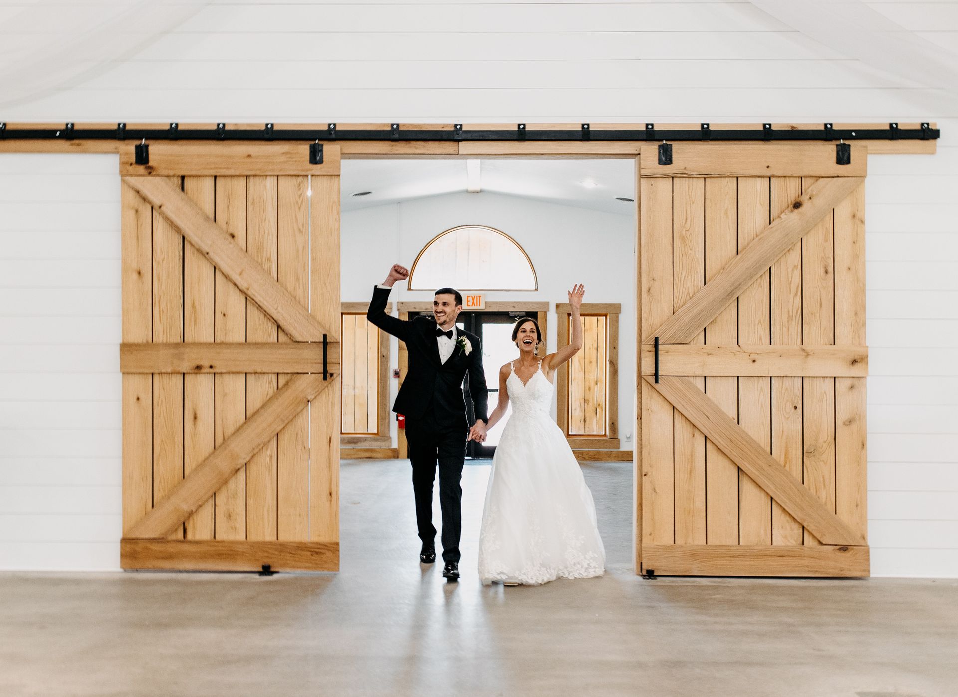 A bride and groom are walking through a barn doorway.