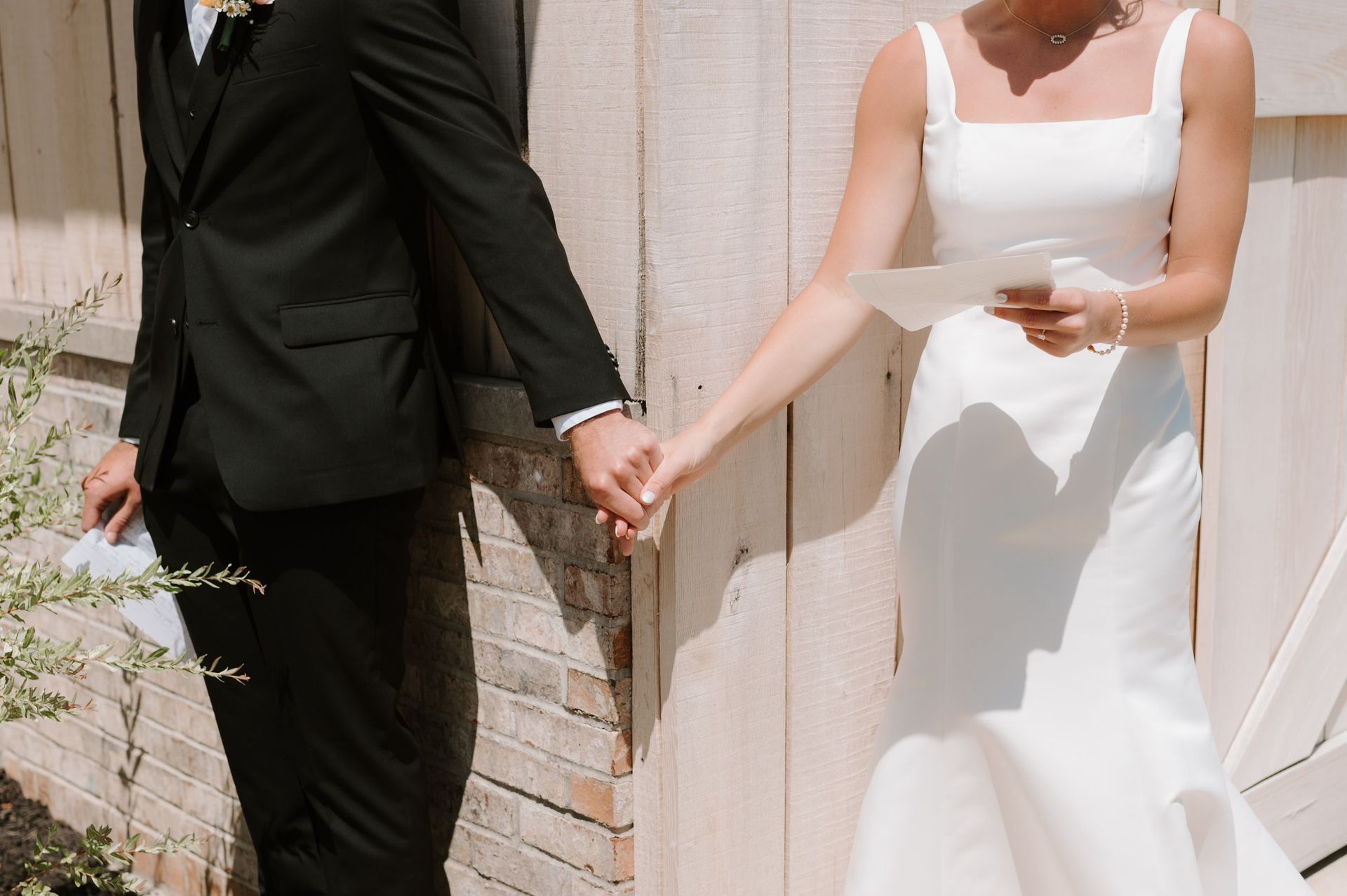 A bride and groom are holding hands in front of a wooden fence.