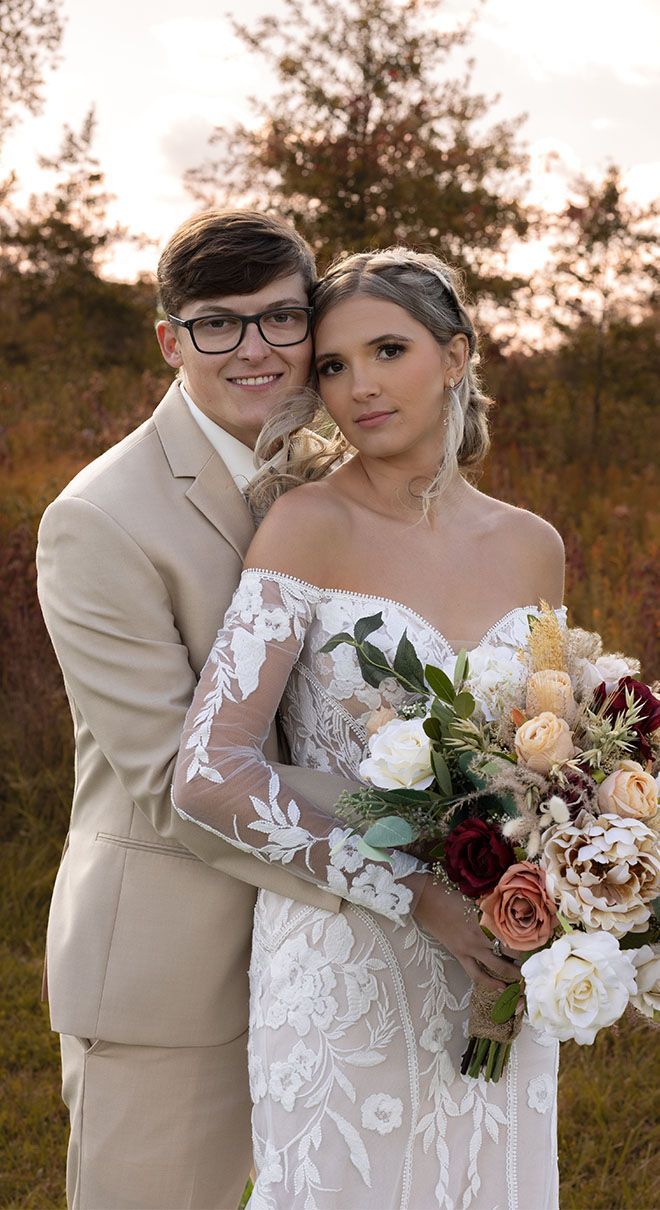 A bride and groom are posing for a picture while the bride is holding a bouquet of flowers.