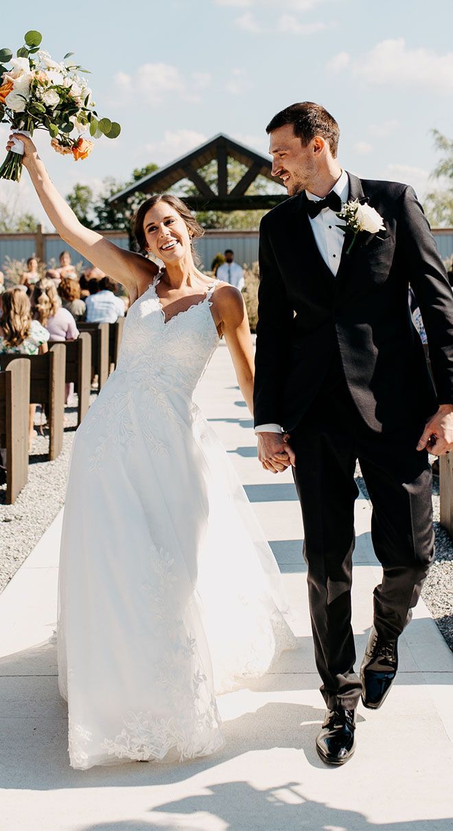 A bride and groom are walking down the aisle holding hands.