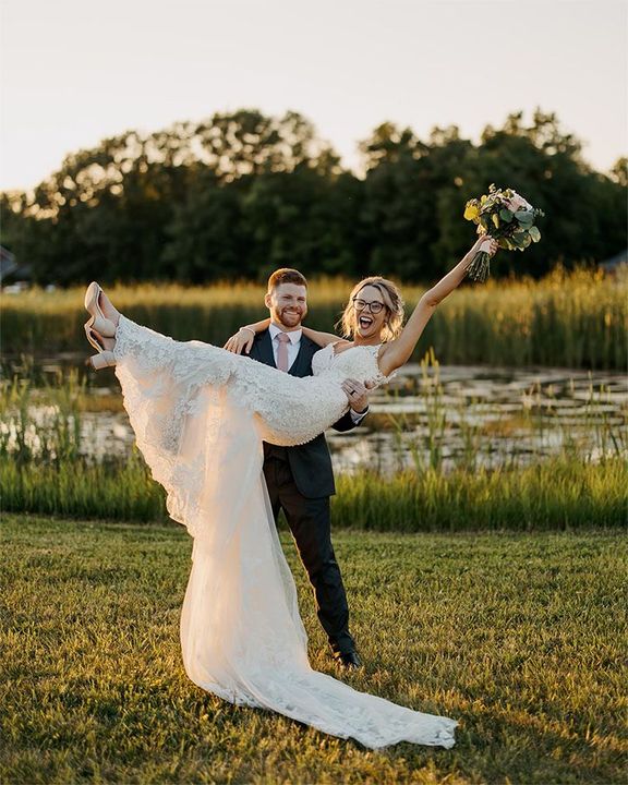 A man is carrying a bride in his arms in a field.