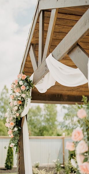 A wooden gazebo decorated with flowers and white cloth for a wedding ceremony.
