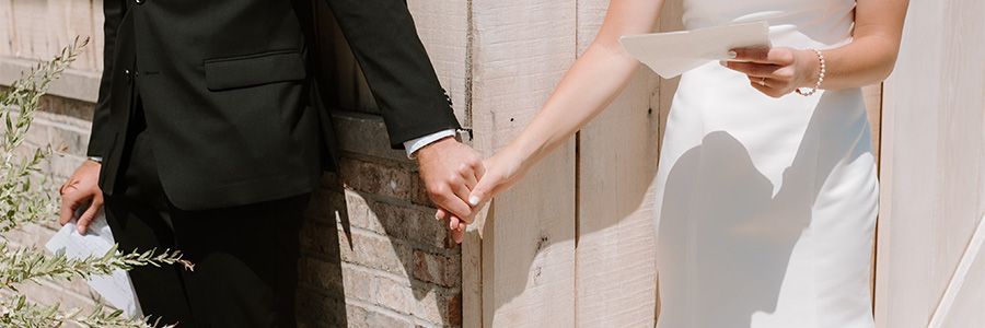A bride and groom are holding hands in front of a wooden fence.