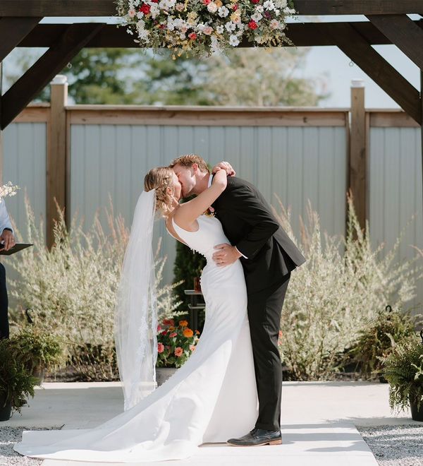 A bride and groom kissing at their wedding ceremony under a pergola.