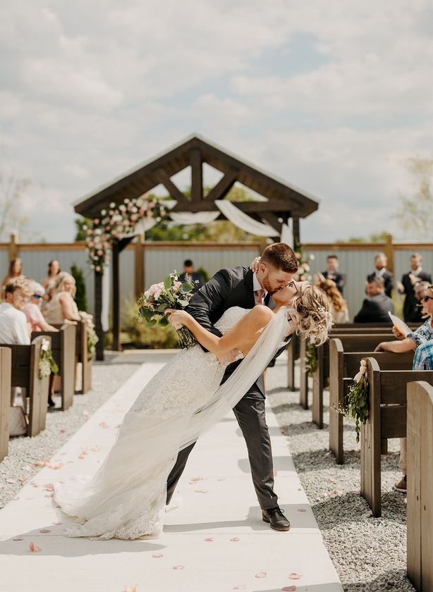 A bride and groom are kissing at their wedding ceremony in front of a church.