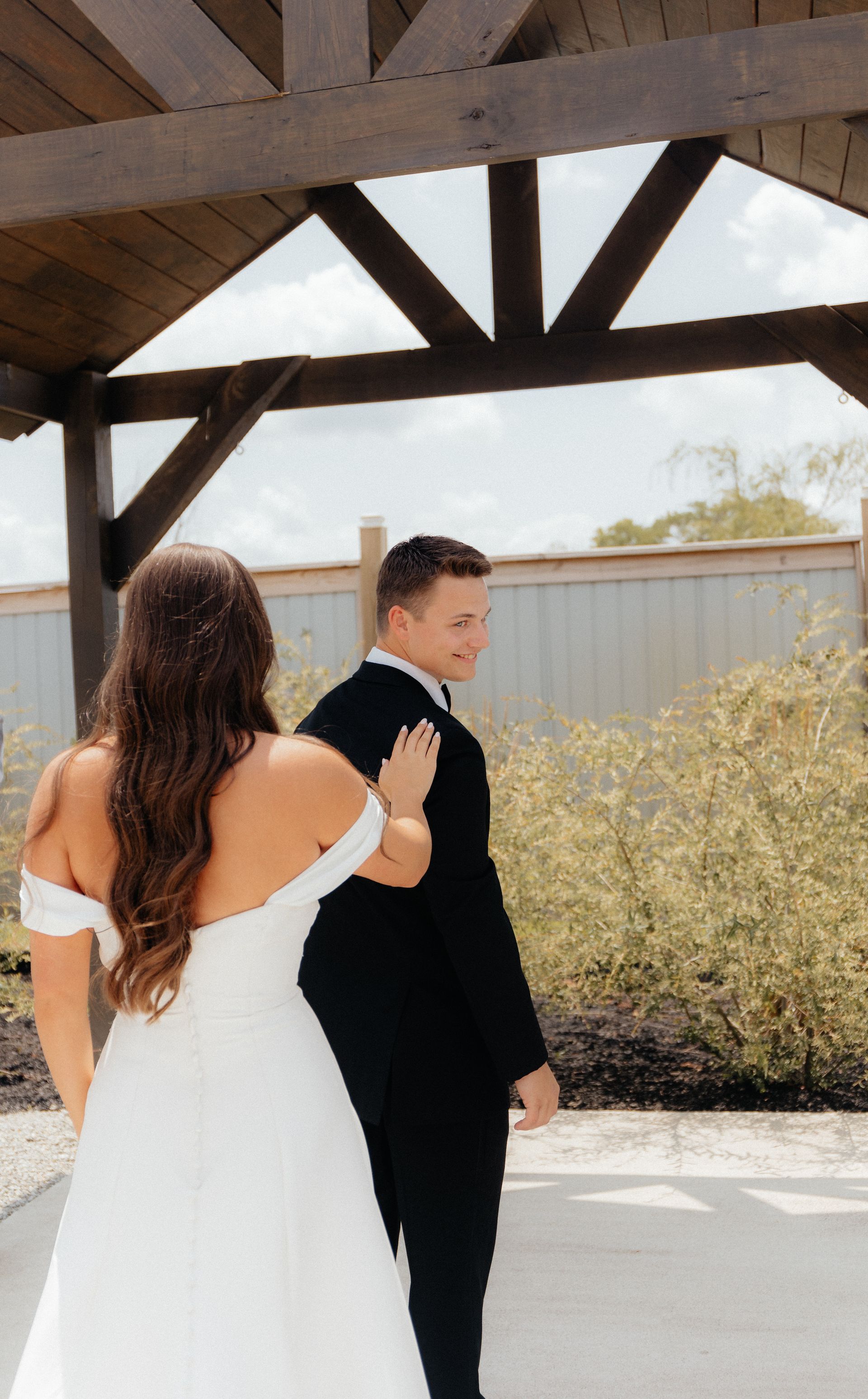 A bride and groom are standing under a wooden structure.