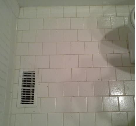 A bathroom floor with white tiles and a vent.