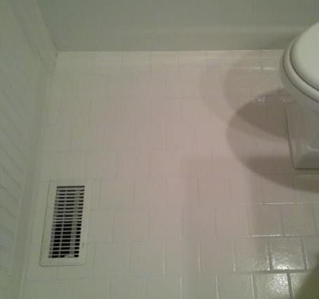 A toilet is sitting on a white tiled floor next to a vent.