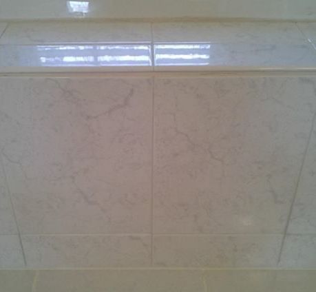 A close up of a white tile wall with a reflection of a window.