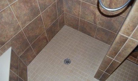 A shower stall with brown tiles and a drain in a bathroom.