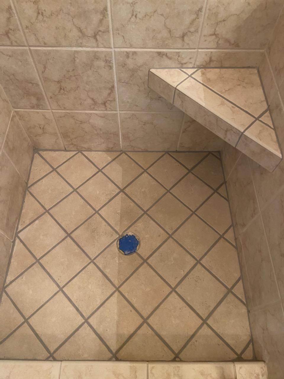 A tiled shower stall with a blue drain and a shelf.