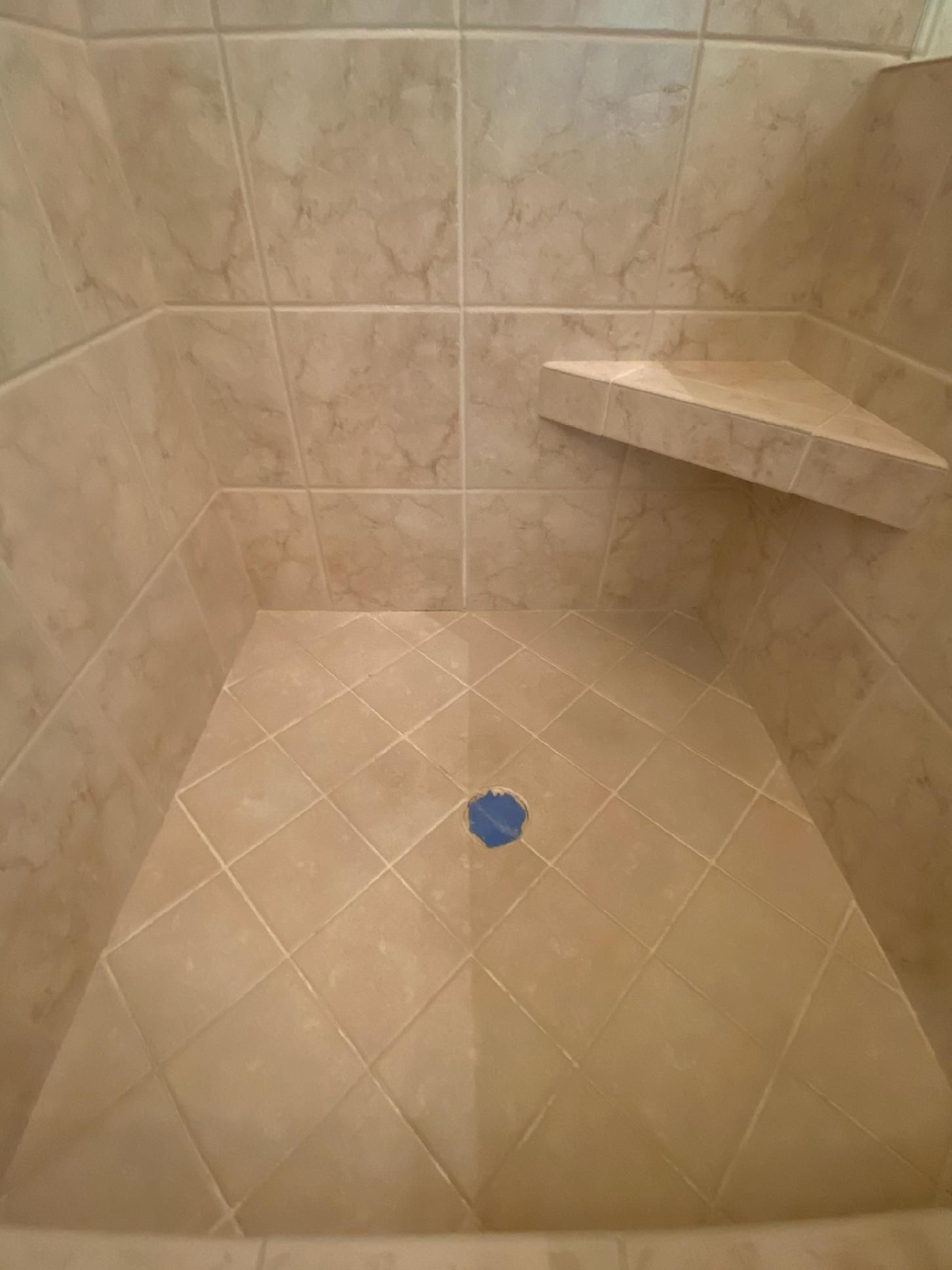 A tiled shower with a corner shelf and a blue drain.