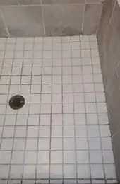 A bathroom floor with white tiles and a toilet in the background