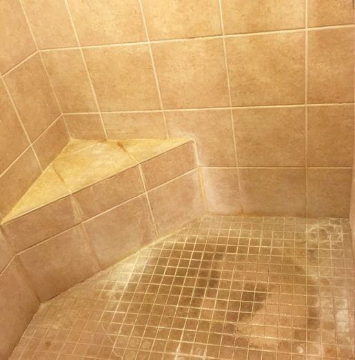 A shower stall with a corner shelf and a tiled floor.