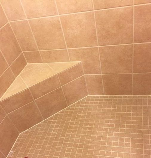 A tiled shower with a corner seat and a tiled floor