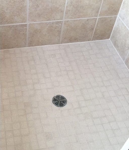 A white tiled shower floor with a drain in the middle.