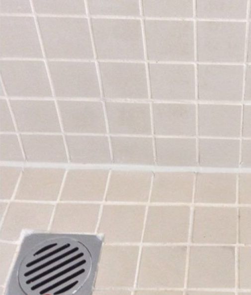 A drain in a bathroom next to a tiled wall.
