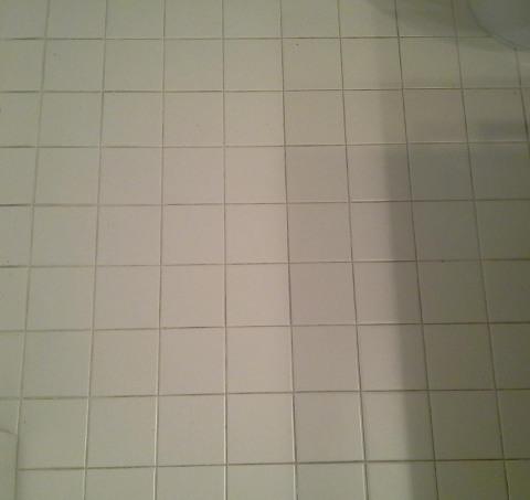 A bathroom floor with white tiles and a toilet in the background