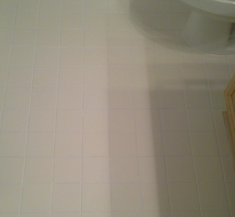 A white tiled floor in a bathroom next to a toilet.