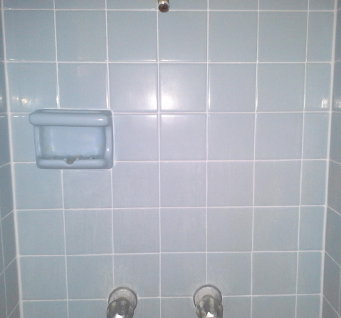 A bathroom with blue tiles and a soap dish on the wall.