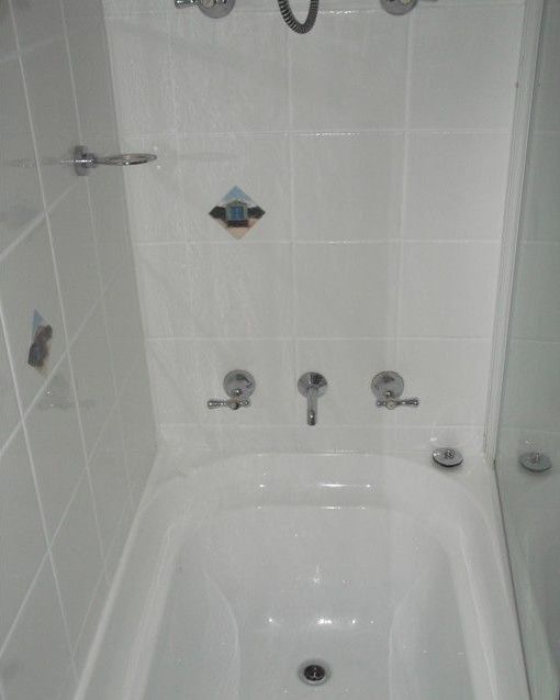 A bathtub in a bathroom with white tiles and chrome faucets.