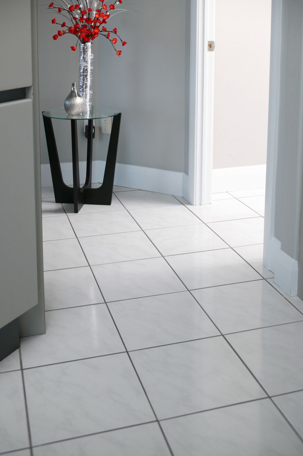 Hallway with white tile floor, table with vase and red flowers, and open doorway.