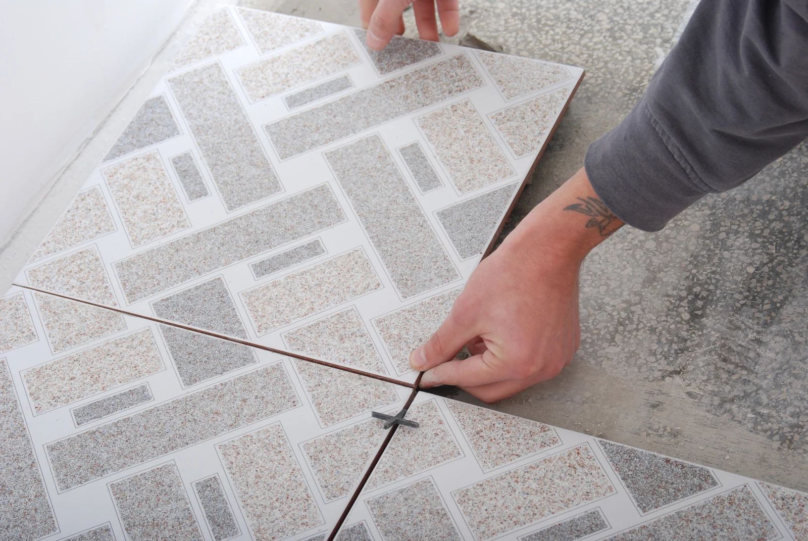 Person installing patterned floor tiles, using spacers to align them.