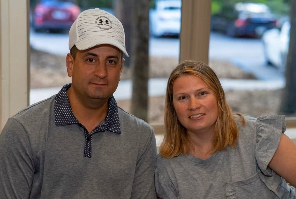 Man wearing a hat and woman smiling, seated indoors.