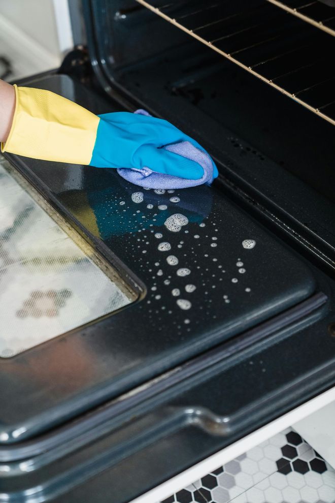 Person wearing a blue and yellow glove cleaning inside of an oven with a wet sponge.