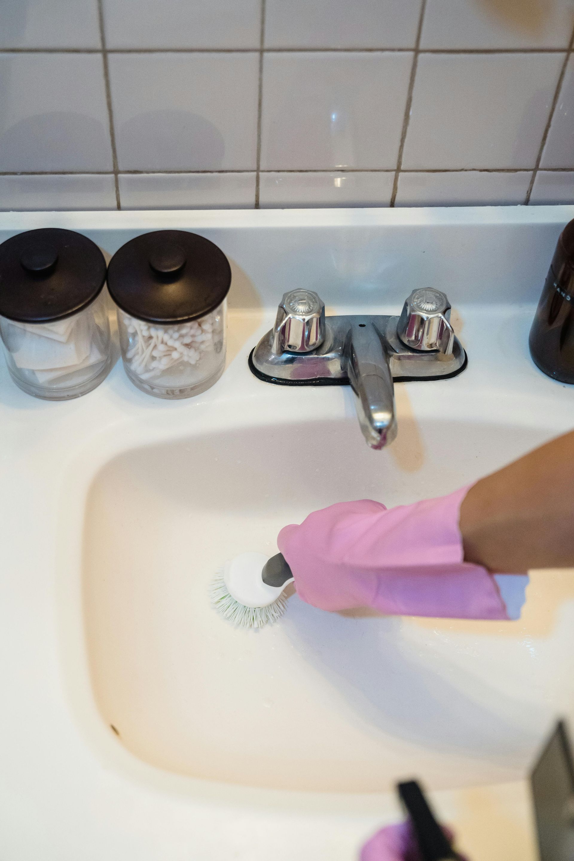 Person wearing pink gloves scrubs a white sink with a brush.