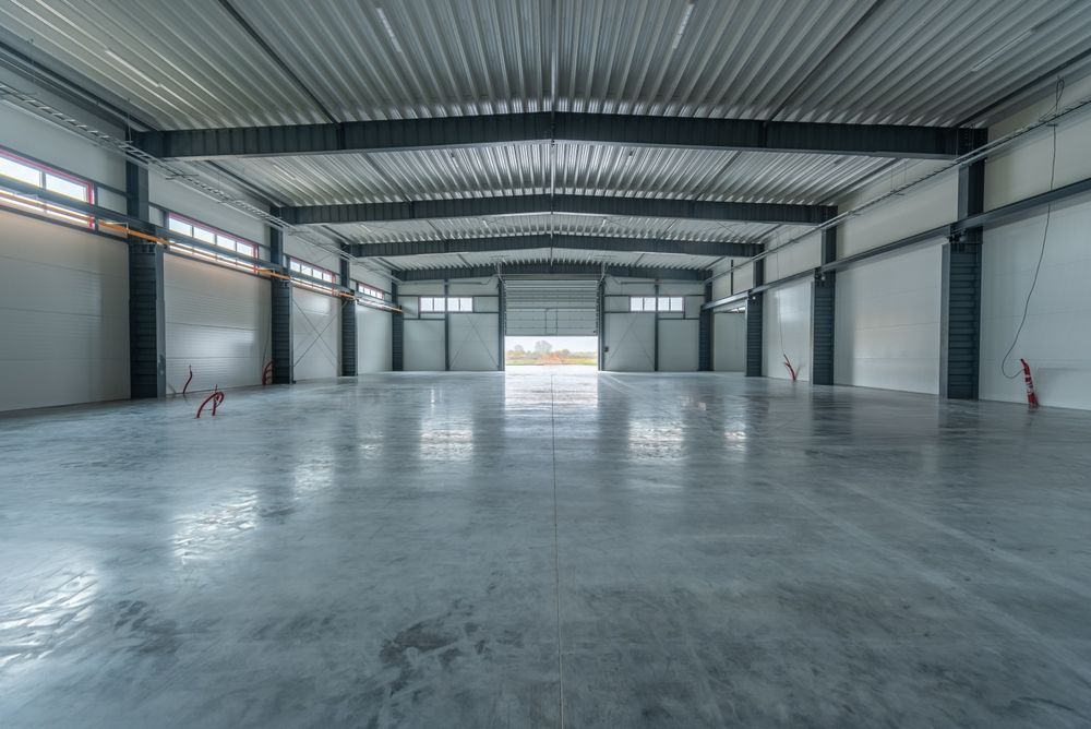 Empty, spacious warehouse interior with polished concrete floor, steel beams, and open loading door.