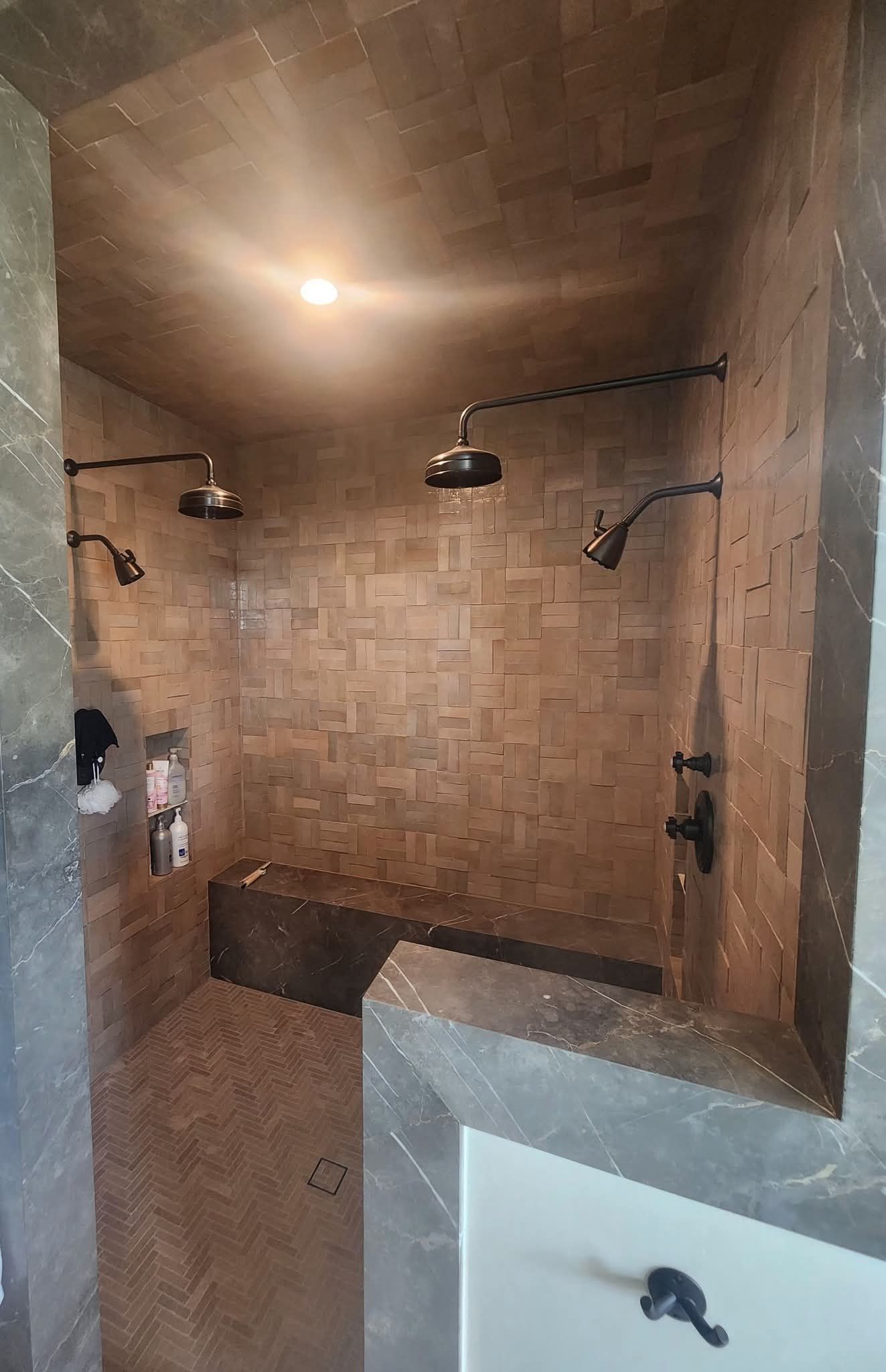 Spacious shower with multiple showerheads. Stone tile walls, built-in bench, dark fixtures.